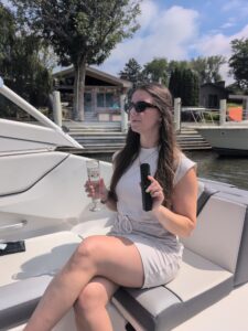 Woman sitting on a boat in a white dress holding mixturus and a glass of water